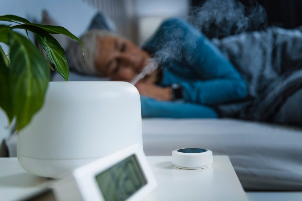 Woman healthy sleeping in bed with an alarm set and air mist diffuser on
