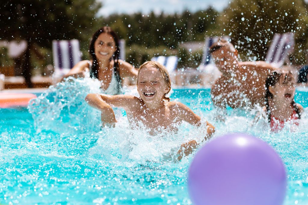 Parents and children laughing while playing ball in swimming pool