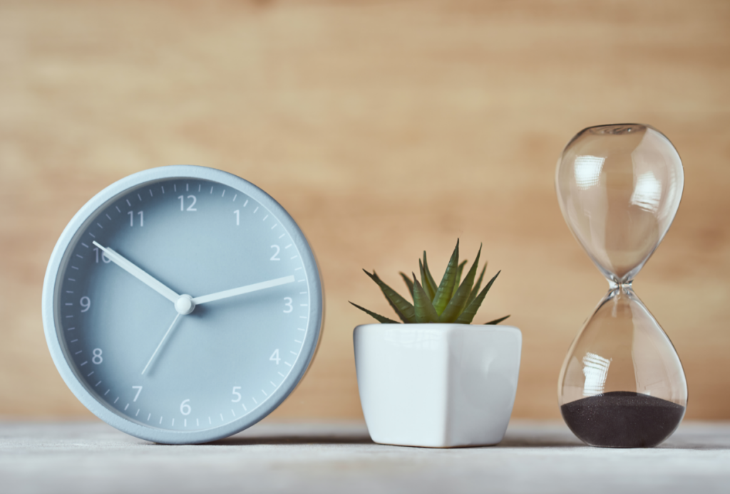 A clock and hourglass depicting the need for time management in order to avoid Medicare late enrollment penalties