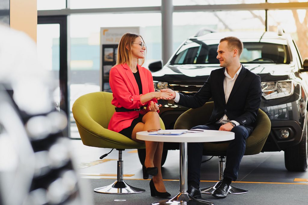 Woman shaking hands with a salesman at a car dealership after finalizing the purchase of her new car.