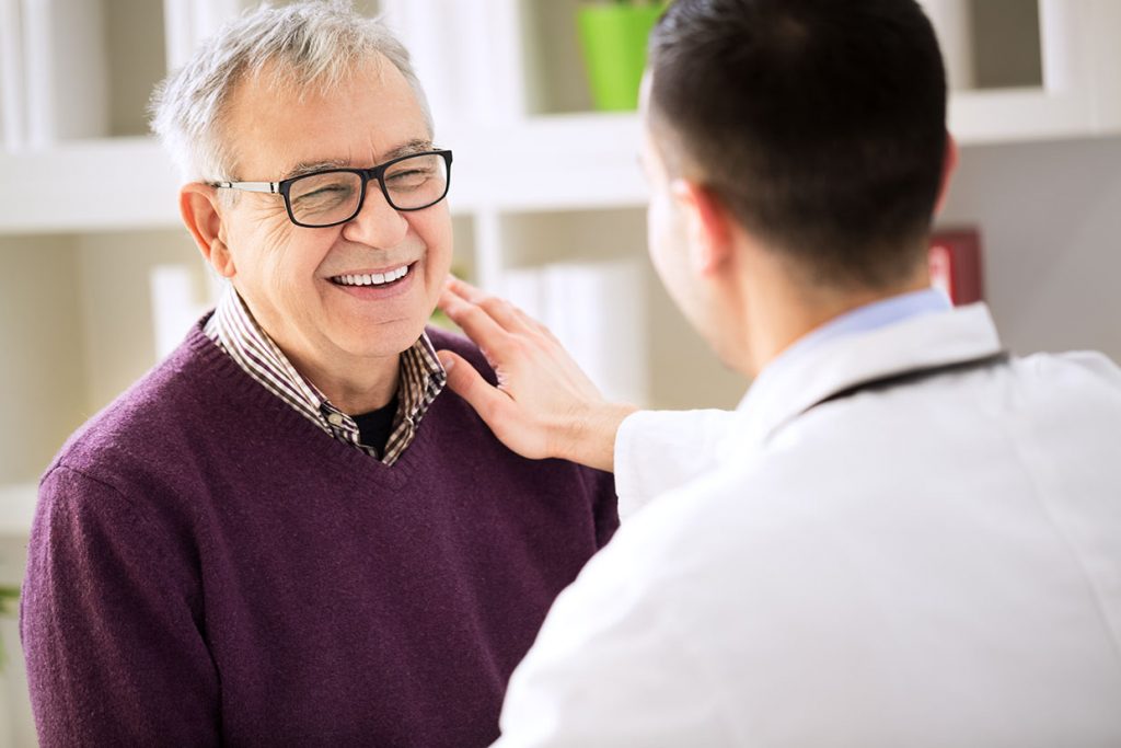 A senior gentleman smiling while speaking with his primary care physician.