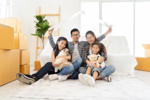 Young family smiling after getting a homeowners insurance policy. They are holding up a roof shaped covering to represent homeowners insurance coverage.