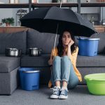 Pensive brunette girl sitting on floor with umbrella and buckets of water.