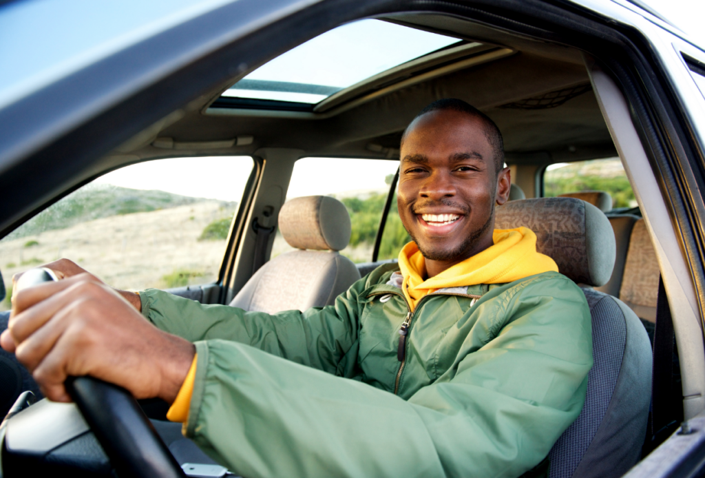 A smiling male driver sitting confidently behind the wheel of his car on a sunny day, feeling happy and assured because he knows he's safeguarded with the right car insurance coverage.
