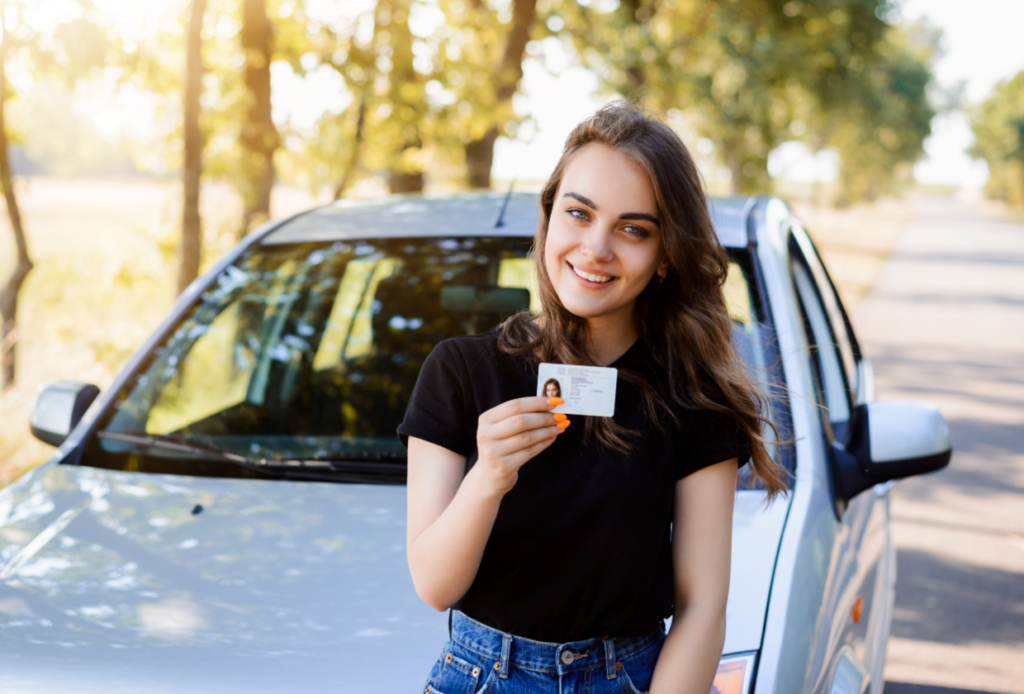 Proud young girl standing in front of her car after getting her drivers license and securing car insurance coverage.