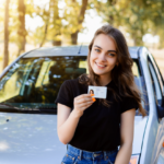 Proud young girl standing in front of her car after getting her drivers license and securing car insurance coverage.